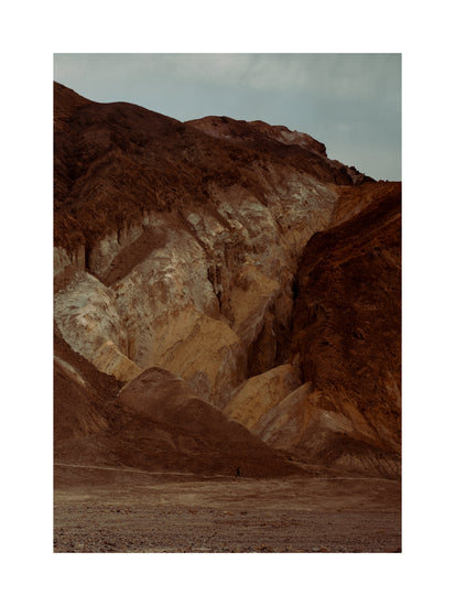 Tiny man walking along the bottom of a massive brown and beige mountain.