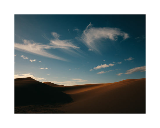 Dessert landscape with brown sand dunes under a clear blue sky.