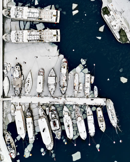 Cargo ship laying white on a dark sea covered in cracked ice.