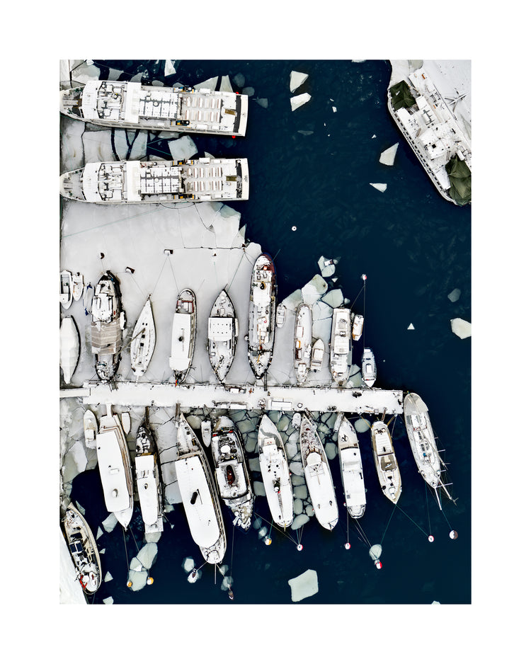 Cargo ship laying white on a dark sea covered in cracked ice.