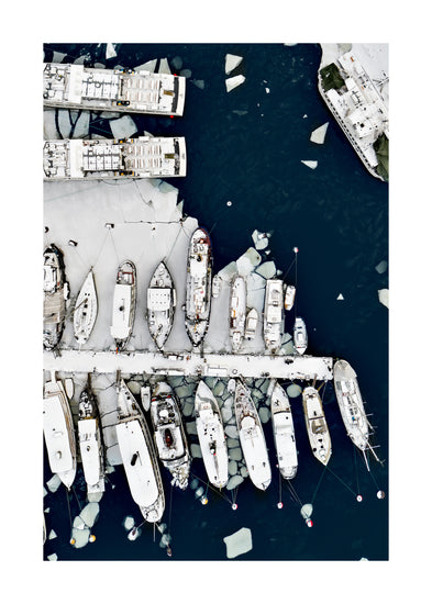 Cargo ship laying white on a dark sea covered in cracked ice.