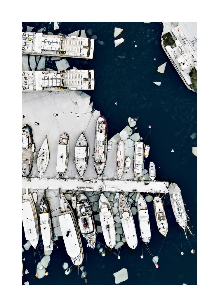 Cargo ship laying white on a dark sea covered in cracked ice.