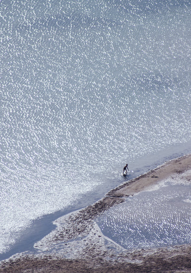 Boy playing in the shallows of a big sea that is sparkling in the sunlight.
