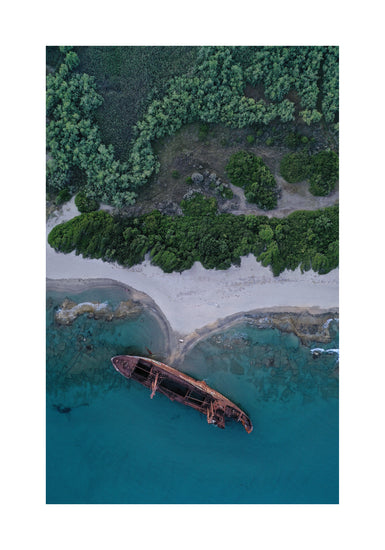 A shipwreck washed up on shore laying between the blue ocean and a green forest.
