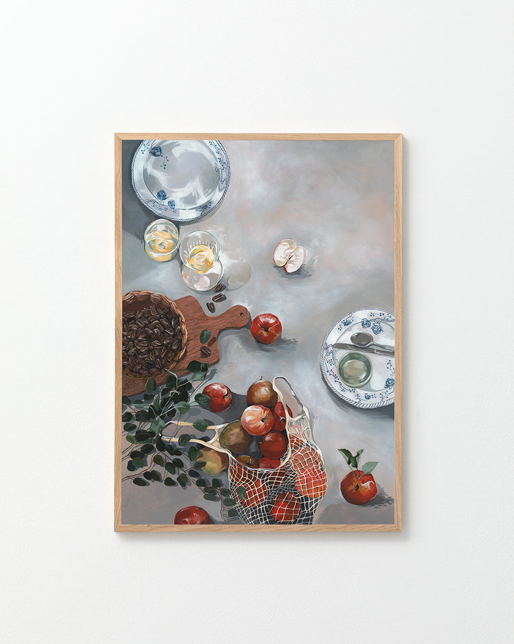 The How Do You Like These Apples Poster showcases a still life scene with red apples, a basket, plates, a cutting board, herbs, a cracked egg, and nuts on a gray tabletop for warm decor and rustic coziness.