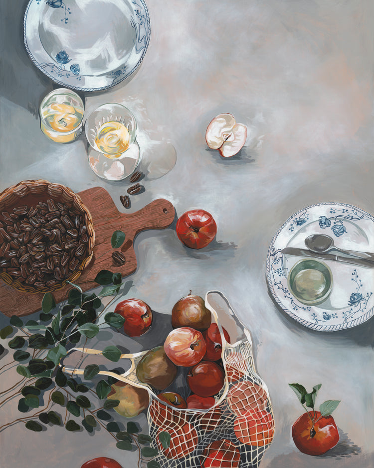 The How Do You Like These Apples Poster showcases a kitchen table set with warm decor: a basket of red apples, a wooden board with pecans, two plates including one holding a green egg-shaped object, two half-filled glasses, scattered apple pieces, and a leafy branch spilling over the side.