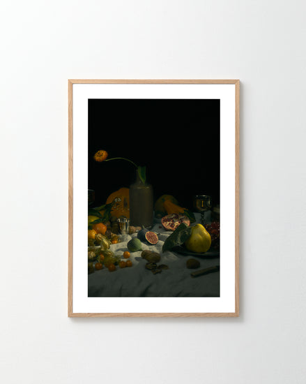 The Gloomy Picnic I Poster, inspired by Paul Cézanne, showcases a dark background with fruits, vegetables, a floral ceramic jug, and more on a table. Reminiscent of art photography, it hangs elegantly on a plain white wall.