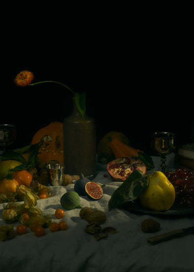 Still life photograph of fruits and flowers on a white canvas.