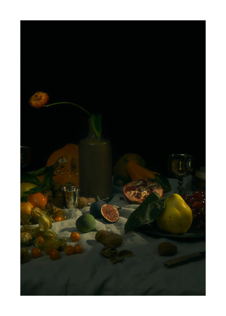 Still life photograph of fruits and flowers on a white canvas.