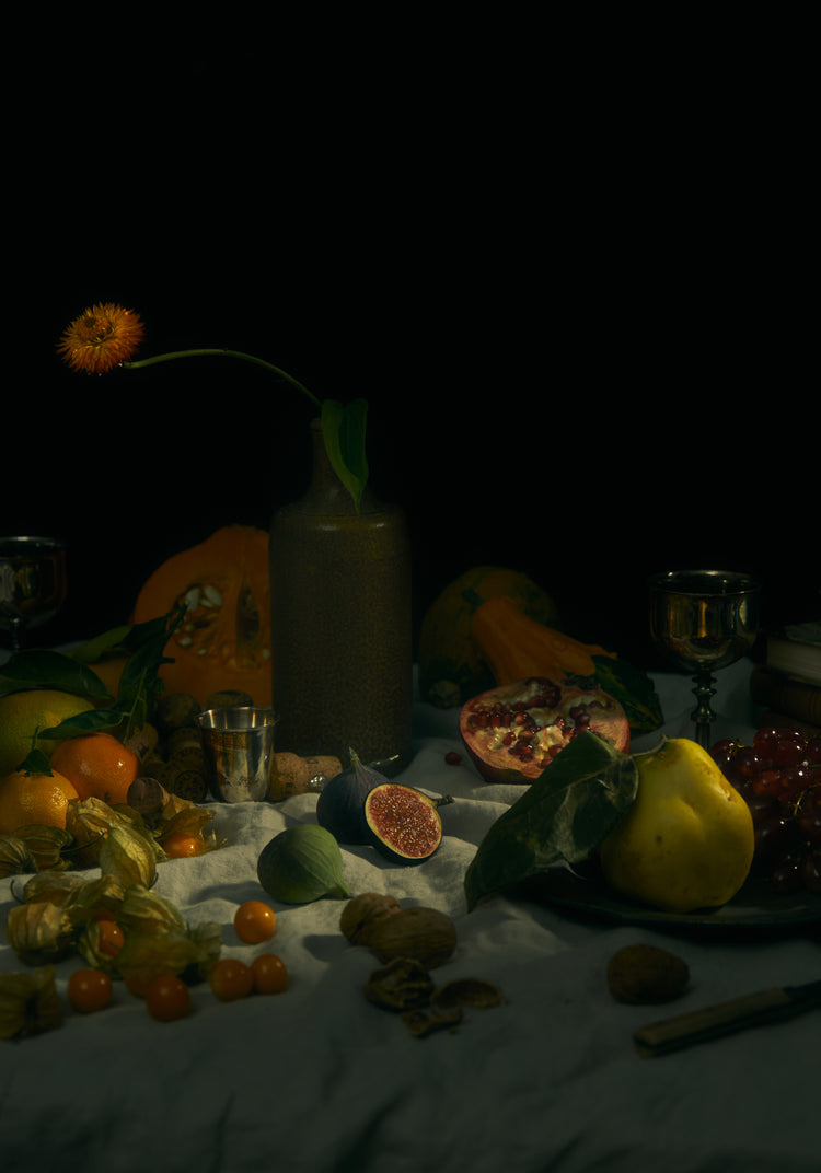 Still life photograph of fruits and flowers on a white canvas.