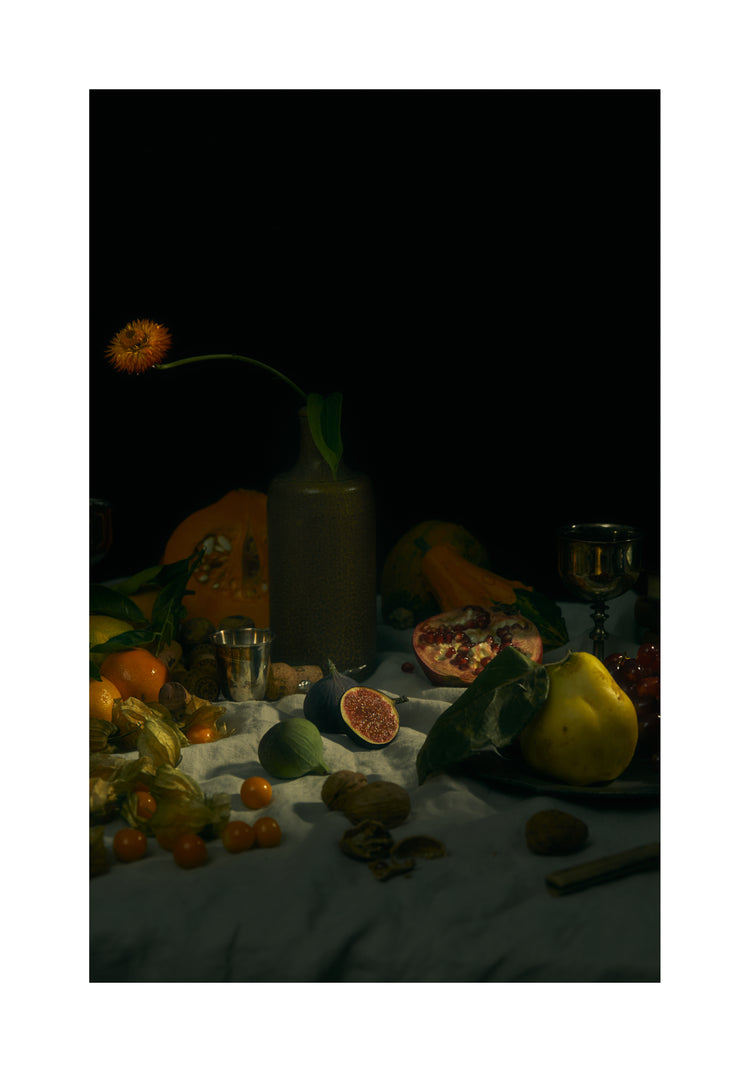 Still life photograph of fruits and flowers on a white canvas.