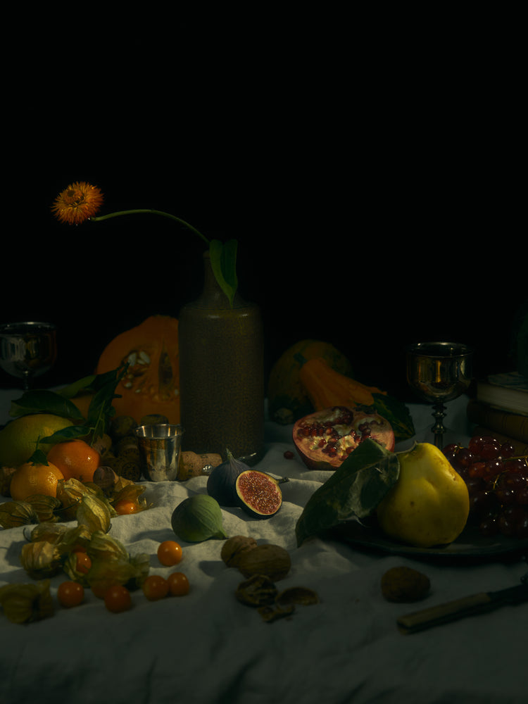 Still life photograph of fruits and flowers on a white canvas.