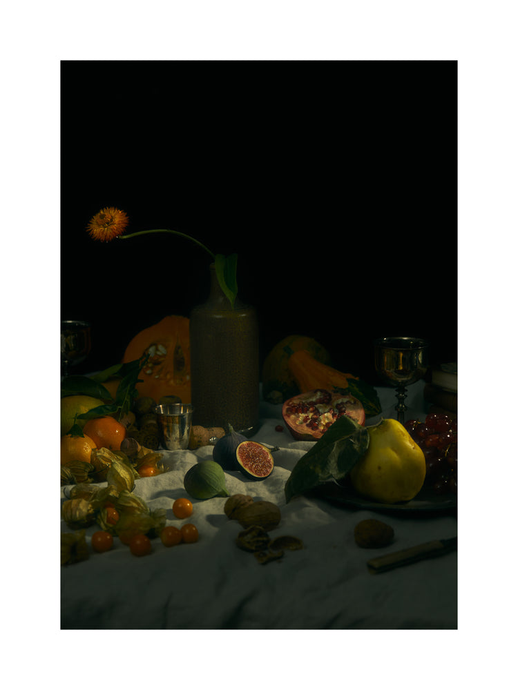 Still life photograph of fruits and flowers on a white canvas.