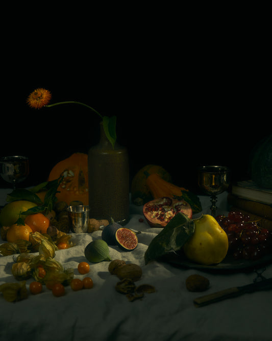 Still life photograph of fruits and flowers on a white canvas.