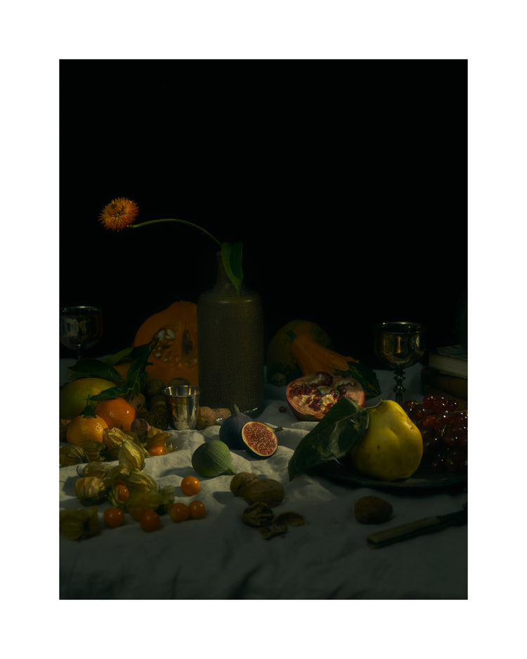 Still life photograph of fruits and flowers on a white canvas.