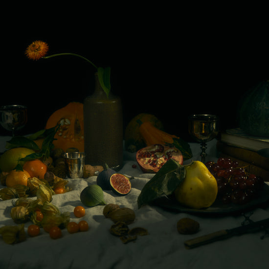 Still life photograph of fruits and flowers on a white canvas.