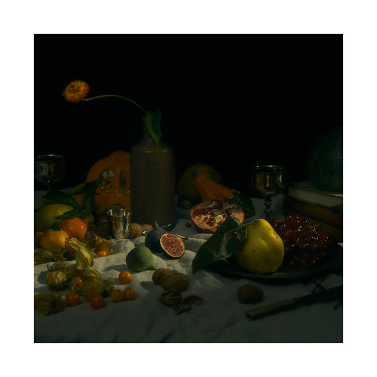 Still life photograph of fruits and flowers on a white canvas.