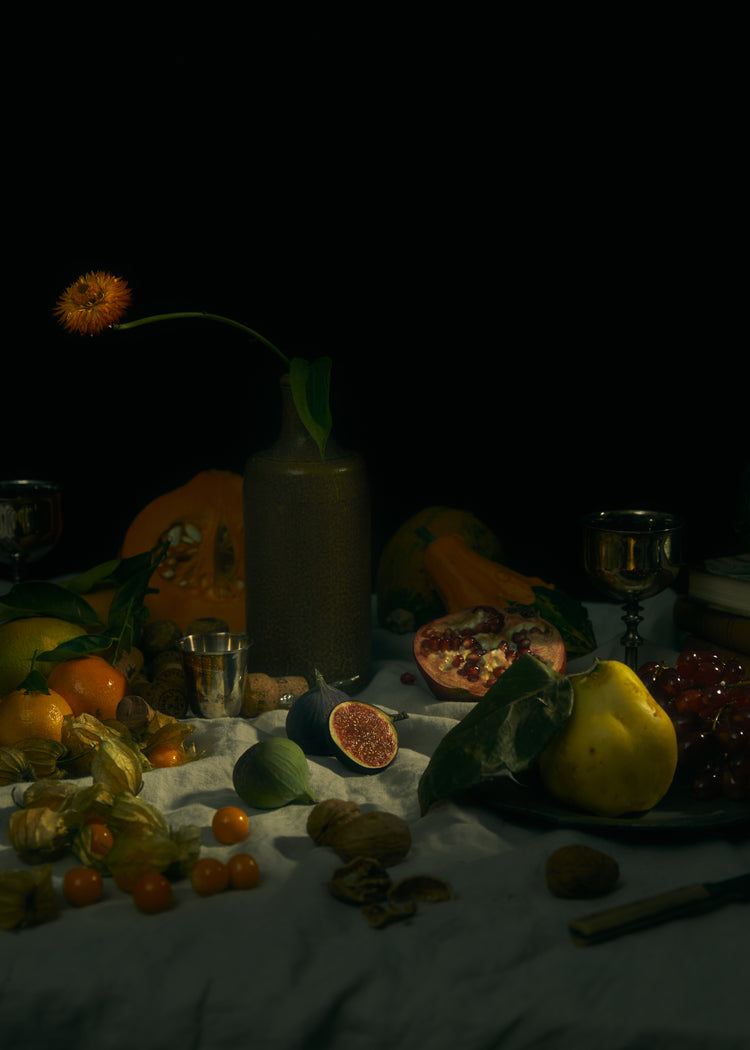 Still life photograph of fruits and flowers on a white canvas.