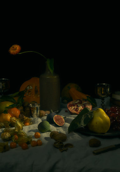 Still life photograph of fruits and flowers on a white canvas.