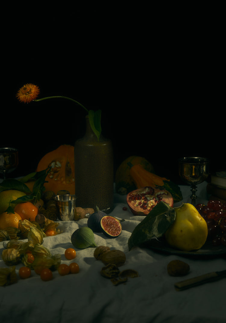 Still life photograph of fruits and flowers on a white canvas.