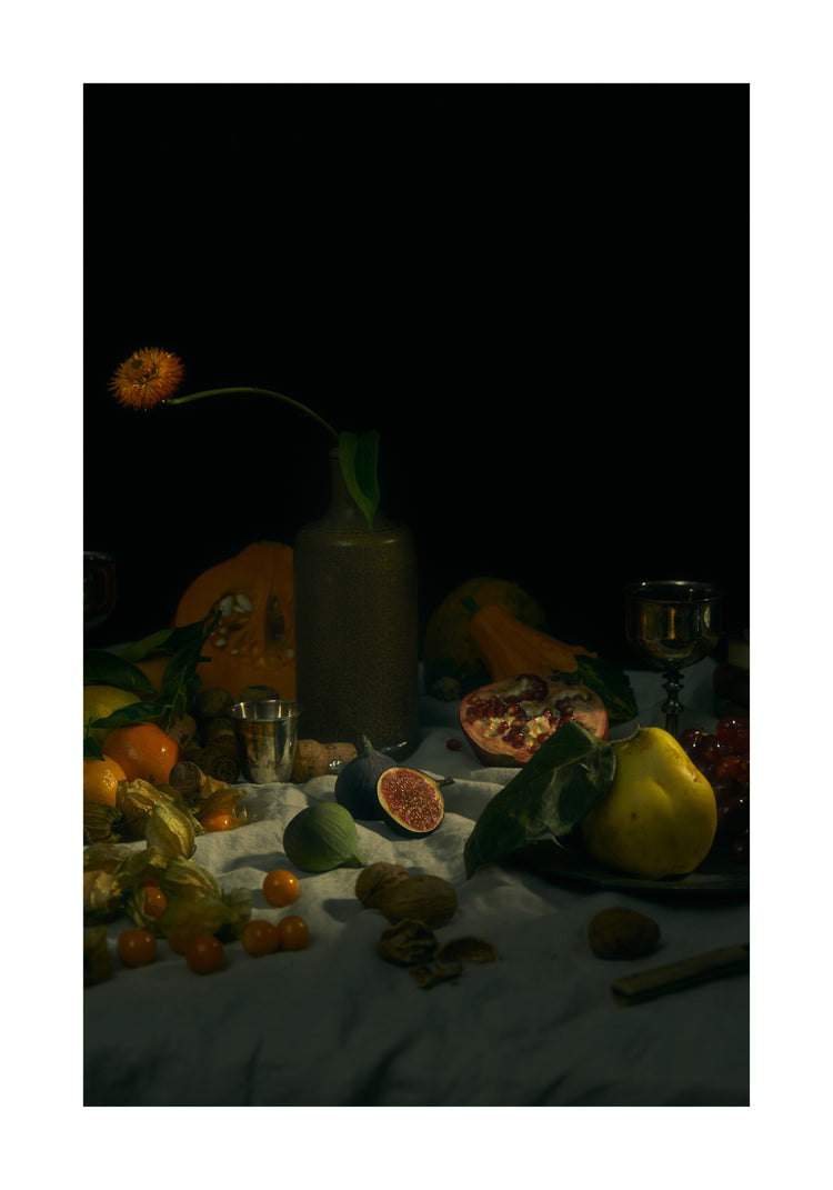 Still life photograph of fruits and flowers on a white canvas.