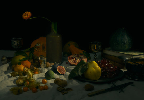 Still life photograph of fruits and flowers on a white canvas.