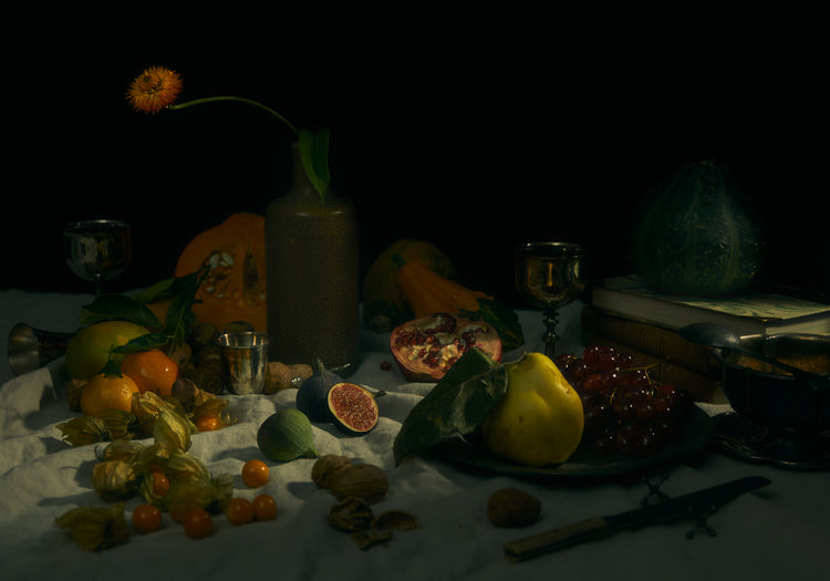 Still life photograph of fruits and flowers on a white canvas.