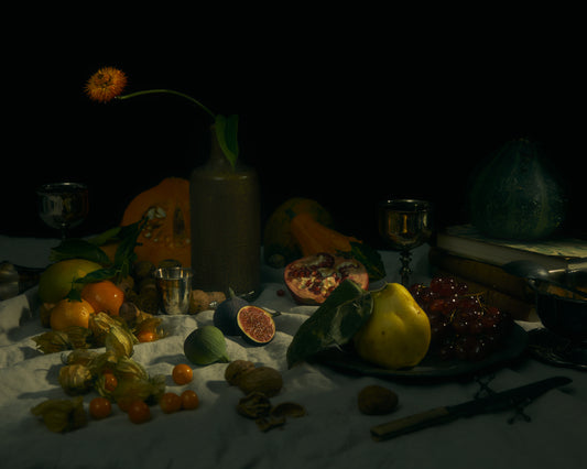 Still life photograph of fruits and flowers on a white canvas.