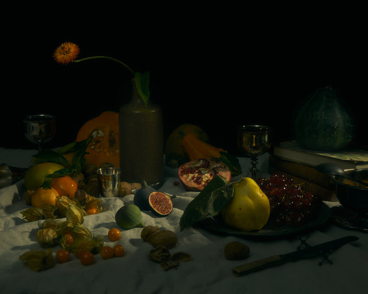 Still life photograph of fruits and flowers on a white canvas.