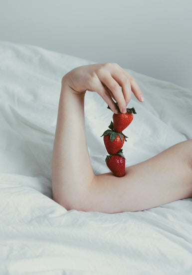 Female arm resting on a sheet with three strawberries stacked on her skin.