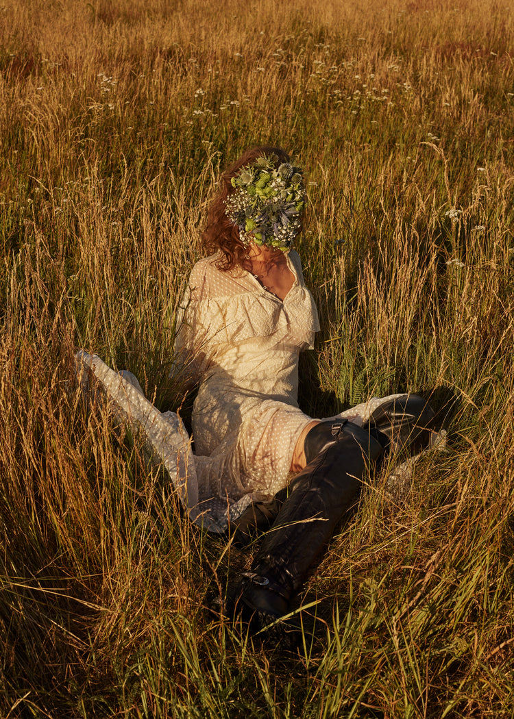 Woman portrayed on a summer meadow with a face mask made of flowers.