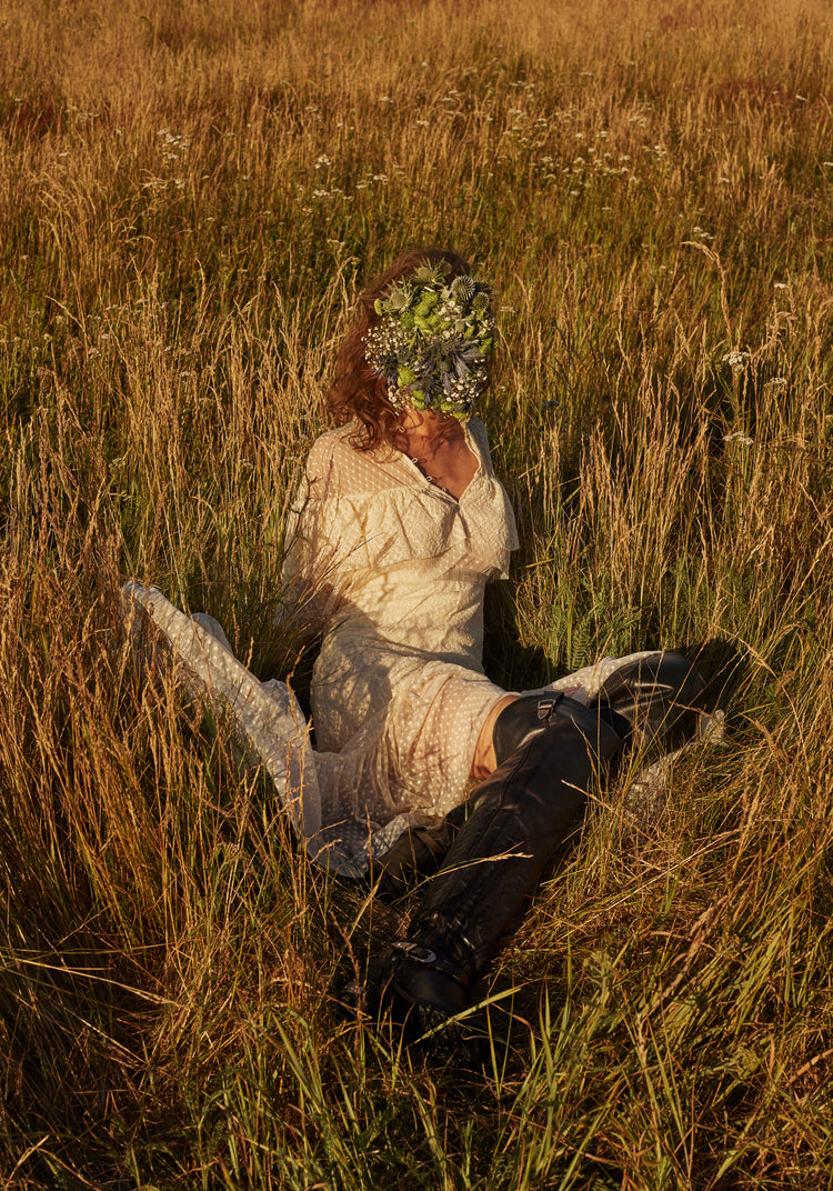 Woman portrayed on a summer meadow with a face mask made of flowers.
