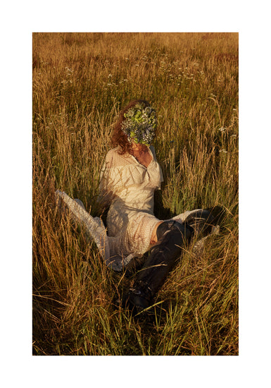 Woman portrayed on a summer meadow with a face mask made of flowers.