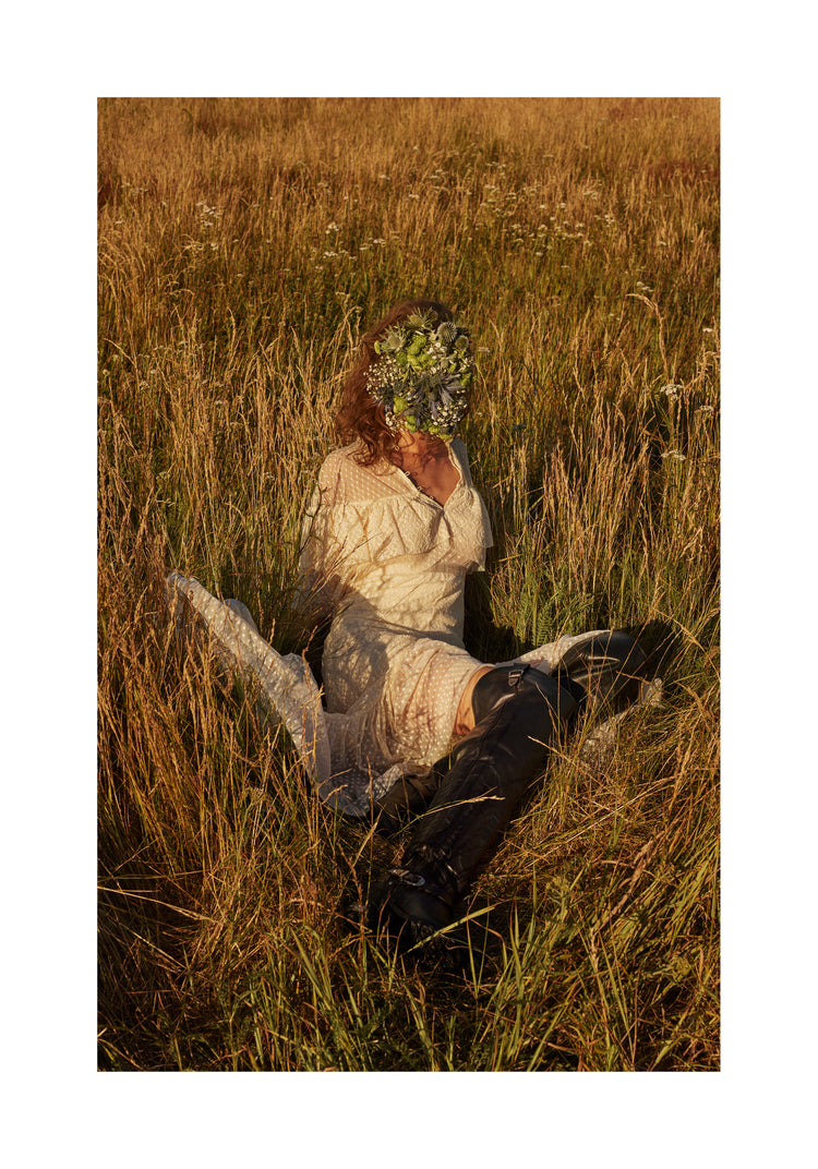 Woman portrayed on a summer meadow with a face mask made of flowers.
