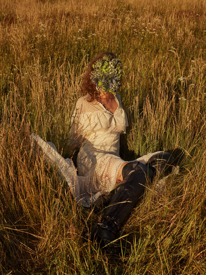 Woman portrayed on a summer meadow with a face mask made of flowers.
