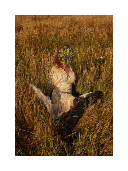 Woman portrayed on a summer meadow with a face mask made of flowers.