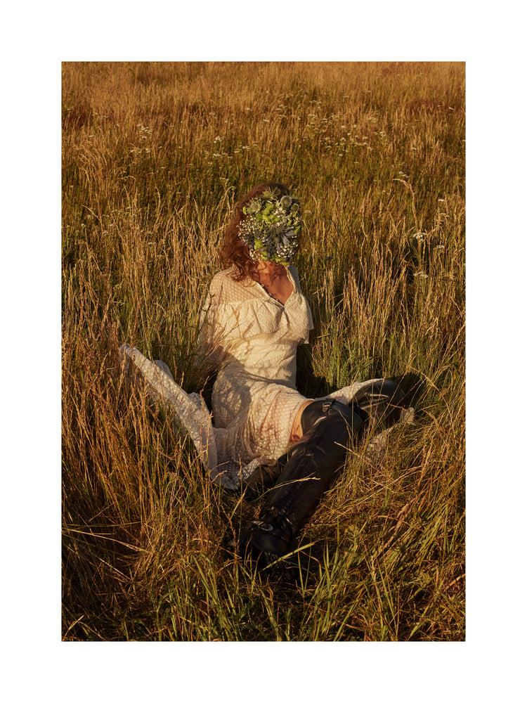 Woman portrayed on a summer meadow with a face mask made of flowers.