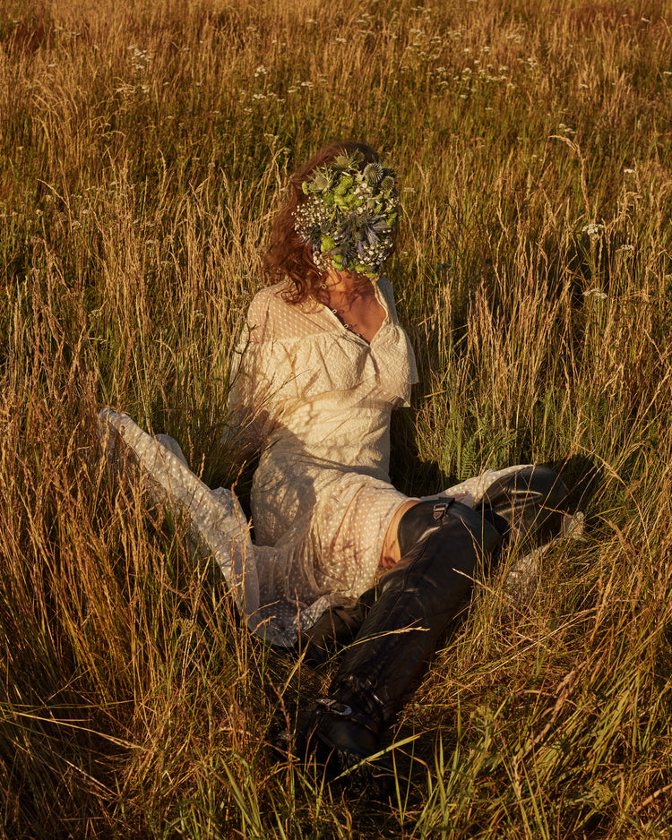 Woman portrayed on a summer meadow with a face mask made of flowers.