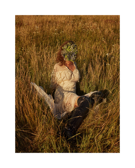 Woman portrayed on a summer meadow with a face mask made of flowers.