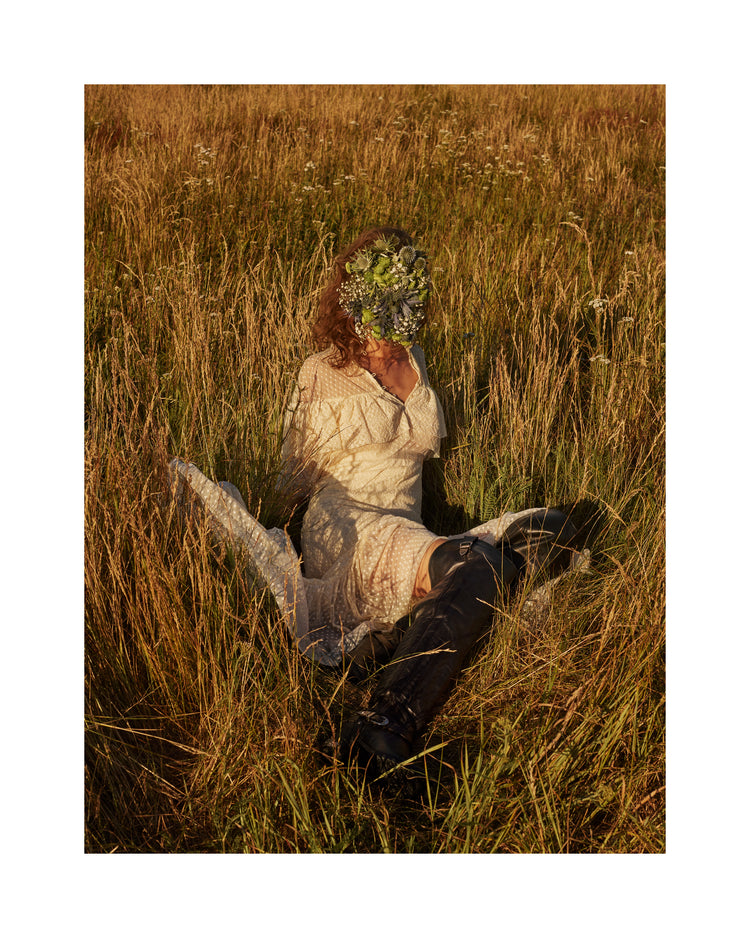 Woman portrayed on a summer meadow with a face mask made of flowers.