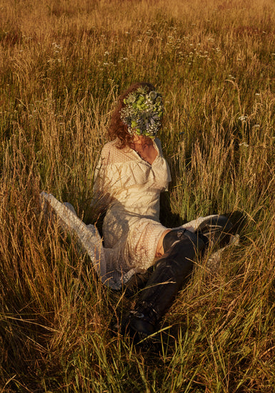 Woman portrayed on a summer meadow with a face mask made of flowers.