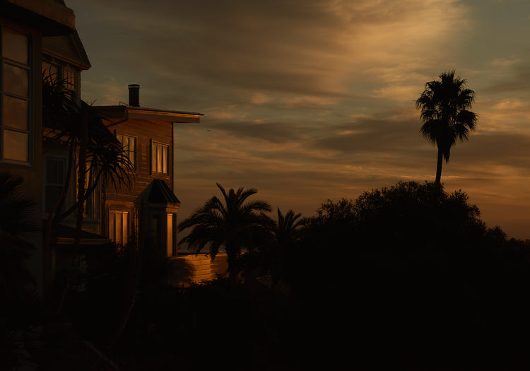 Sunrise glow illuminating a house and turning palm trees into black silhouettes.