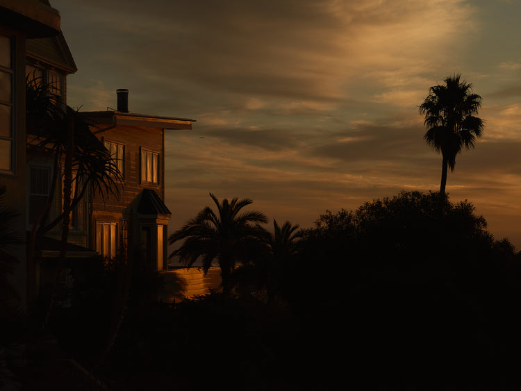 Sunrise glow illuminating a house and turning palm trees into black silhouettes.