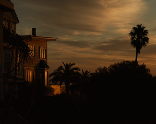 Sunrise glow illuminating a house and turning palm trees into black silhouettes.