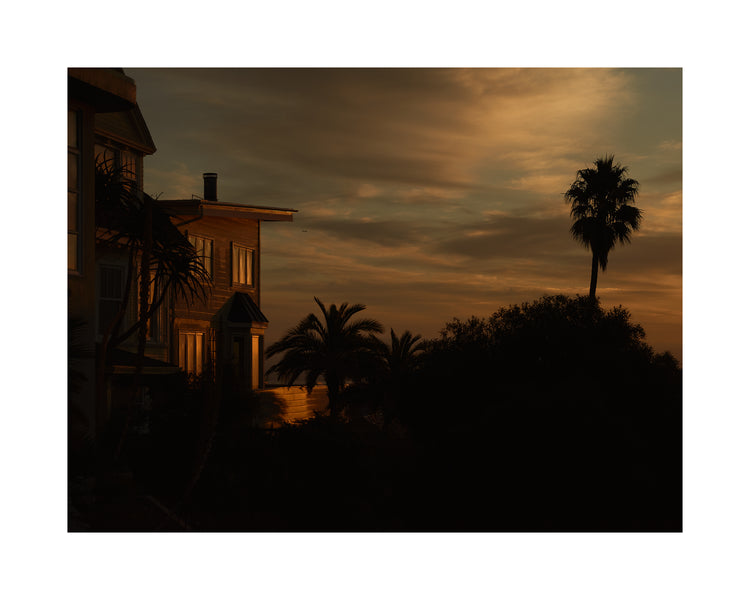 Sunrise glow illuminating a house and turning palm trees into black silhouettes.