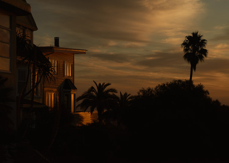 Sunrise glow illuminating a house and turning palm trees into black silhouettes.