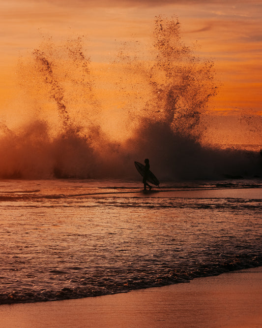 Surfer heading out into the orange waves during sunset.