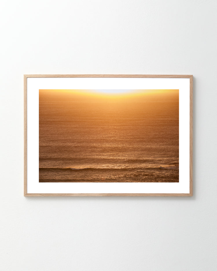The Ikaros Poster showcases a serene ocean scene at sunset, where the sun hovers near the horizon, casting a warm golden glow over the water and creating a peaceful atmosphere.