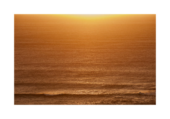 Sun setting over the ocean coloring the water in orange and yellow.