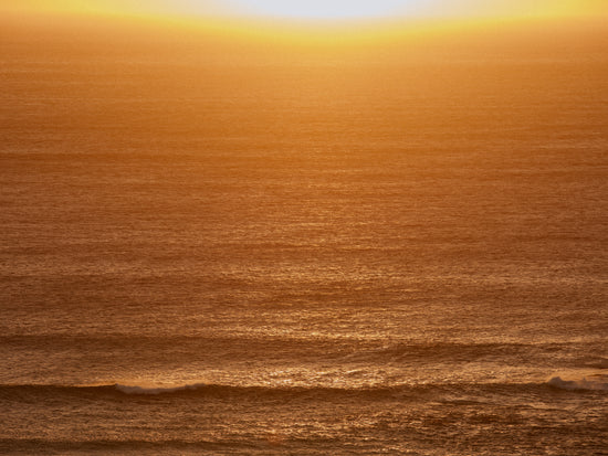 Sun setting over the ocean coloring the water in orange and yellow.